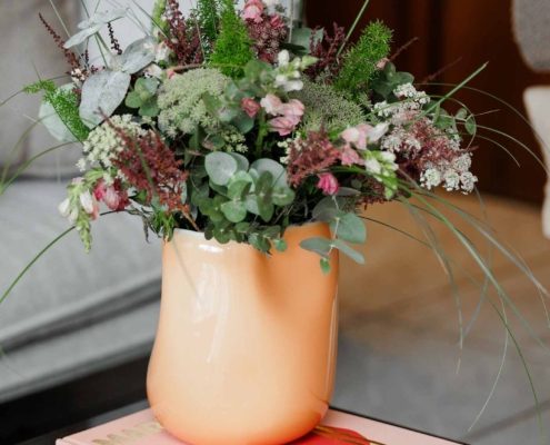 Großer Blumenstrauß Großer Blumenstrauß mit rosa und weißen Blüten, Eukalyptus und Ziergräsern in einer apricotfarbenen Keramikvase auf einem Couchtisch mit Bildband.