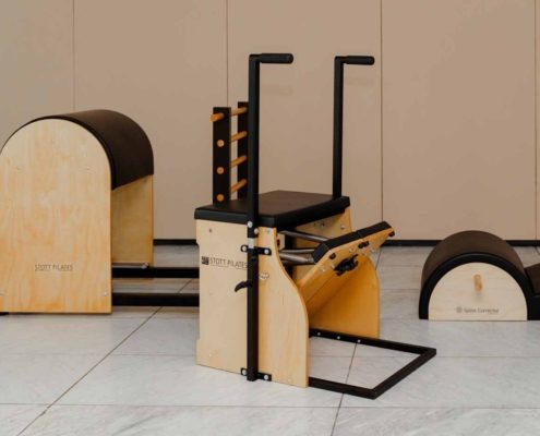 Pilates-Gerät aus Holz und Metall Pilates-Gerät aus Holz und Metall mit gepolsterter Sitzfläche und zwei schwarzen Haltegriffen.