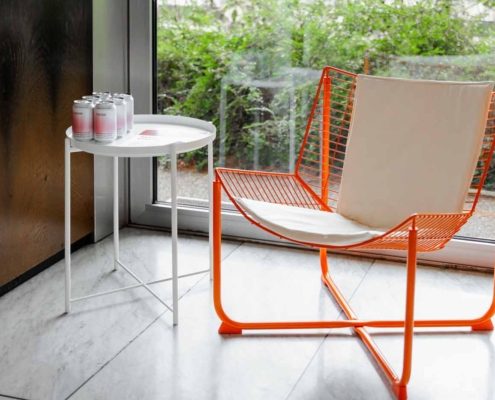 Loungesessel Moderner orangefarbener Loungesessel mit hellem Sitzkissen neben einem weißen Beistelltisch vor einer bodentiefen Fensterfront mit Gartenblick.