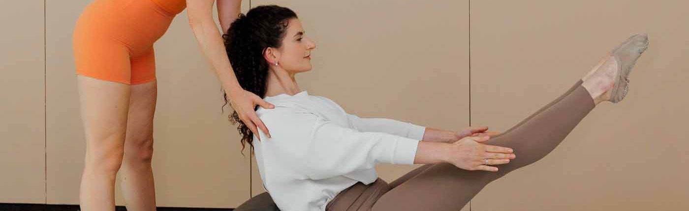 Rückenübung auf dem Spine Corrector Trainerin unterstützt eine Klientin bei einer Rückenübung auf dem Spine Corrector, die Beine in die Luft gestreckt