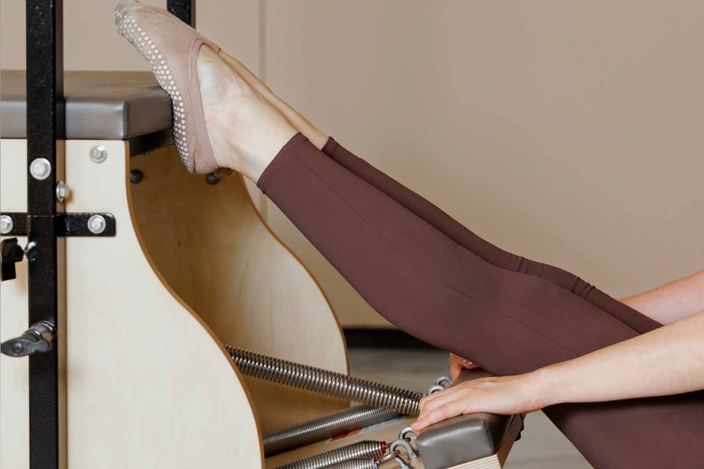 Pilates Stability Chair Nahaufnahme der Füße einer Person in Pilates-Socken auf dem Pedal eines Stability Chair, Hände stabilisieren die Federn